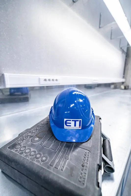 Blauwe veiligheidshelm met het logo van ETI, geplaatst op een gereedschapskoffer in een technische werkomgeving.